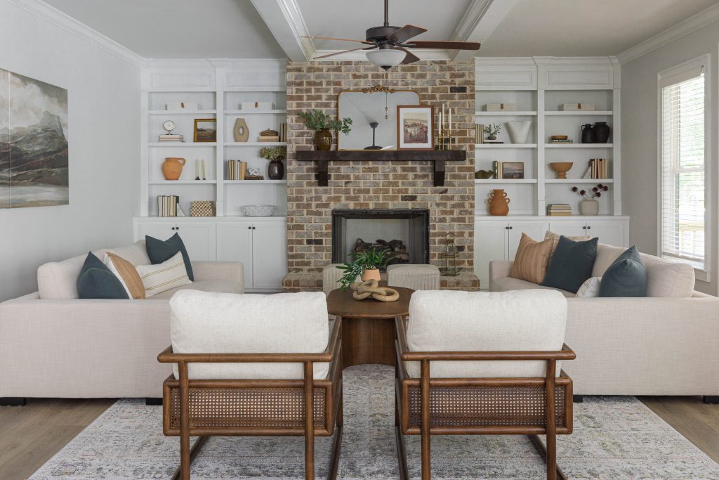 Decorated room in Ford Landing model home with couches, chairs, brick fireplace, and built-in bookshelves