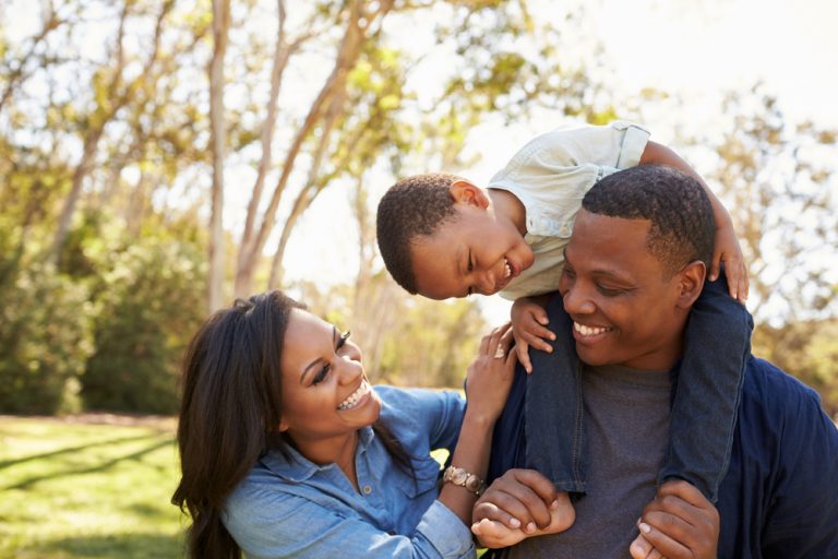 Parents Carrying Son On Shoulders As They Walk In Park ©MonkeyBusinessImages