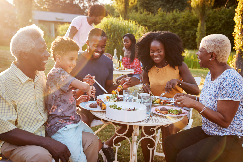 Black multi generation family eating at a table in garden ©Monkey Business