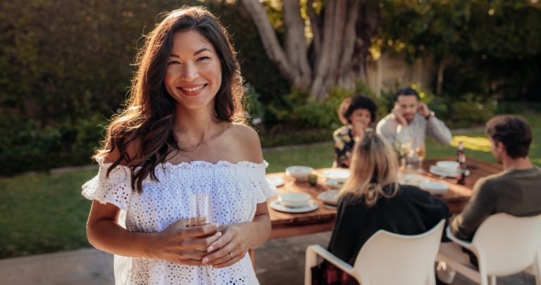 Woman smiling at camera with friends sitting at table in the background