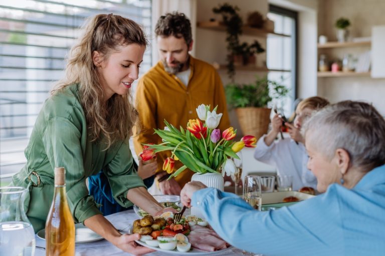 Family Celebrating Easter dinner, daughter holding plate of food for mother ©Halfpoint