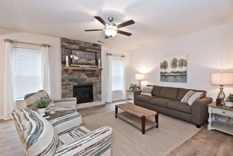 Decorated room with brick fireplace, brown couche, lamps, and patterned loveseats
