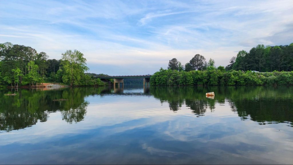 a scenic view of a lake with green trees and a bridge ©Marcus E Jones