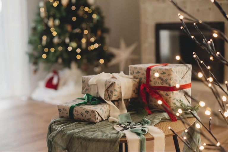 Christmas gifts wrapped with ribbons on a table in front of a decorated Christmas tree with festive lights and ornaments. ©Bogdan Sonjachnyj
