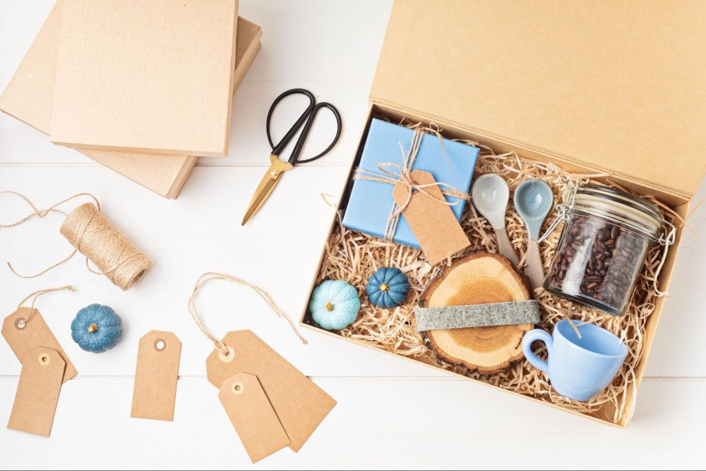 A coffee lover gift box with a mug, wood coaster, measuring spoons, and whole coffee beans. There are scissors and blank name tags next to the box.
©Netrun78