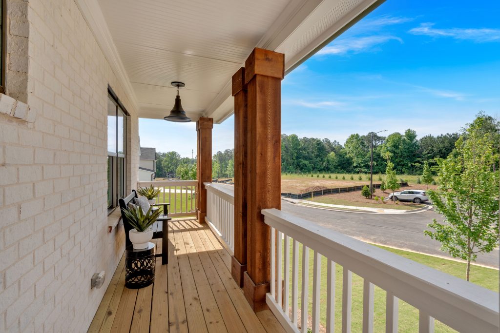 Covered back porch with wooden deck and white railings overlooking a Mableton, GA, community. 