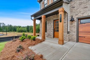 Covered front porch with brick siding and natural wood pillars at a Meadow Pines home in Dallas, GA. 