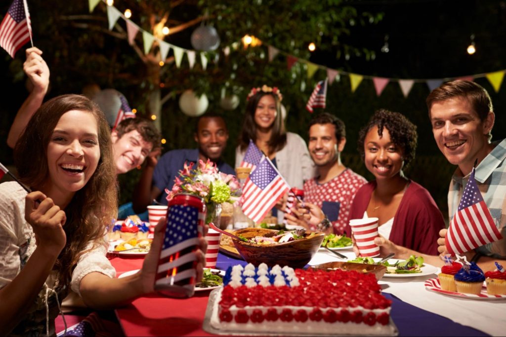 Group of friends smiling and holding small American flags at a 4th of July party in Dallas, GA. ©Monkey Business Images